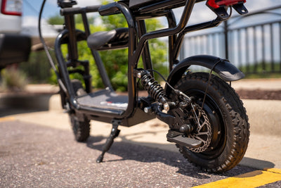 Close-up view of a black EILLEO electric moped showing the rear fat tire, rear shock suspension spring, disc brake system, and folding footrest.